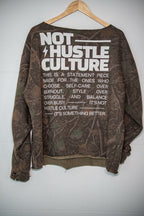 A brown camouflage long-sleeve sweatshirt with a large white graphic text print on the back, hanging on a wooden hanger against a white wall.