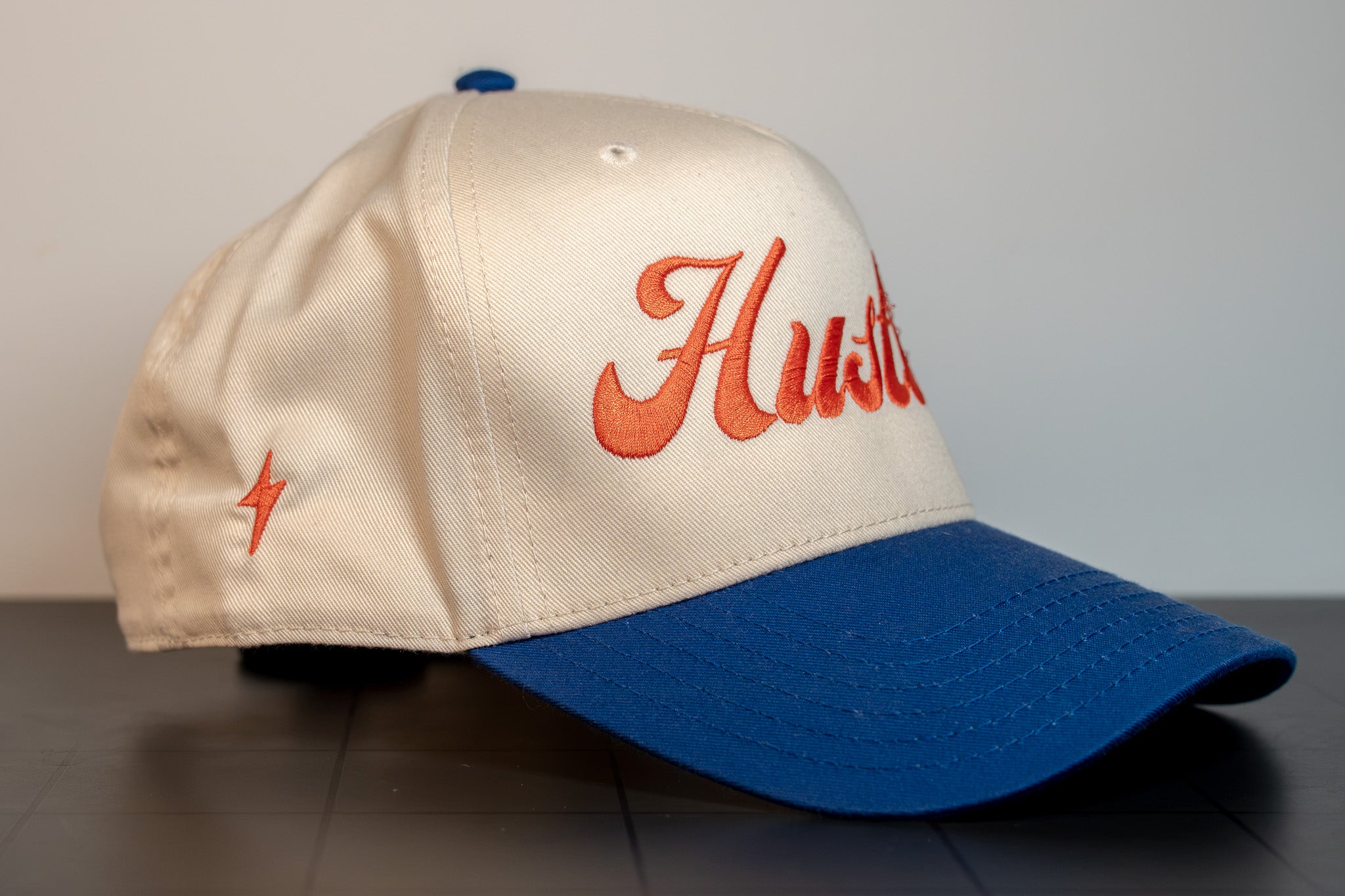 side view of the hustler script cap with the bolt mark on the panel and orange script front