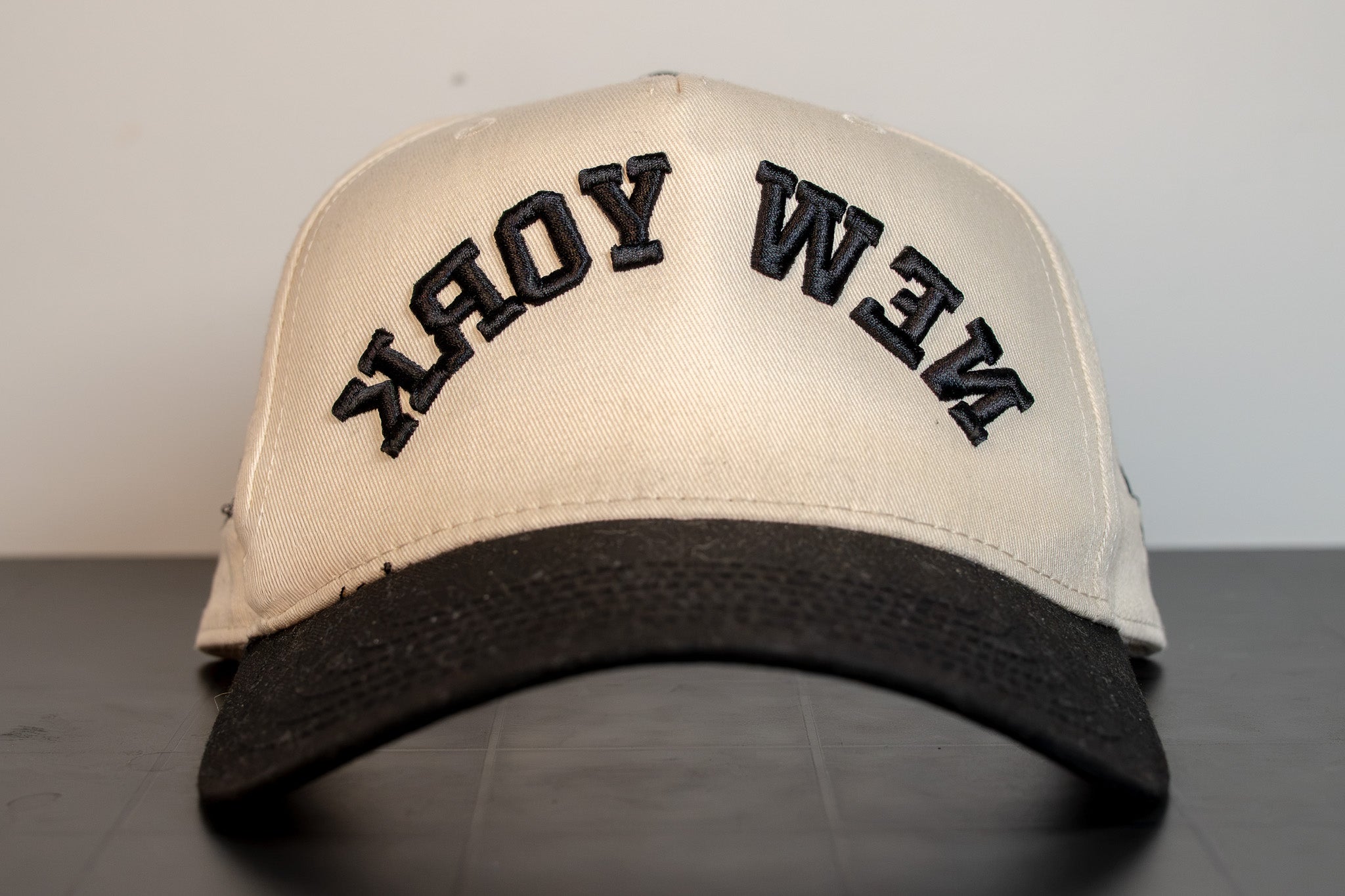 alt: cream cap with black brim and new york arched across the front in black embroidery