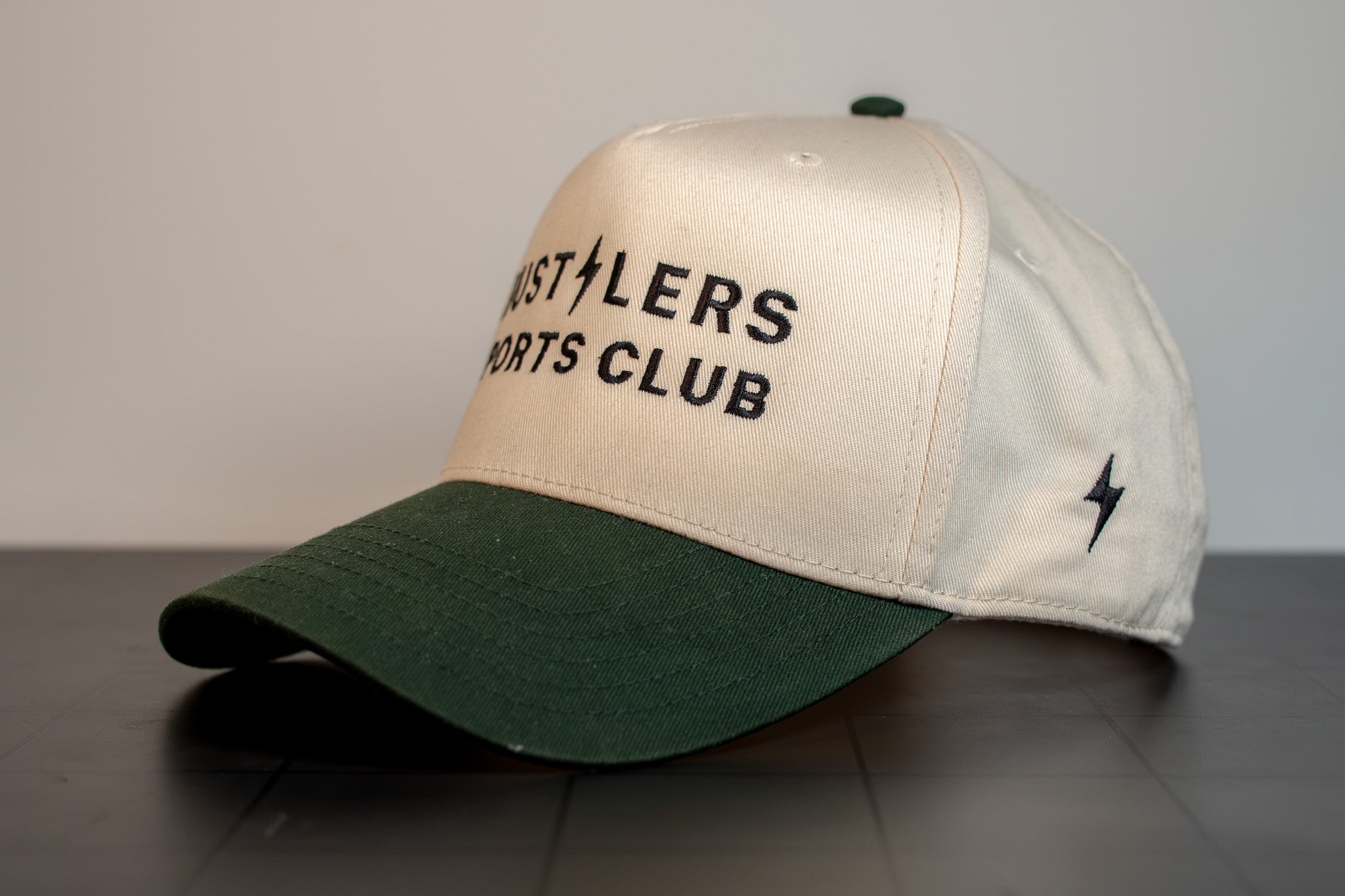 cream cap with forest green brim, hustlers sports club block wordmark and hsc signature on the side panel